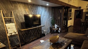 Uma sala de estar aconchegante com piso de madeira, uma TV sobre um móvel, um sofá, uma mesa de centro e um cachorro.