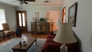 Una sala de estar con una mesa de centro de madera, un sofá rojo, una lámpara y un aparador con adornos.