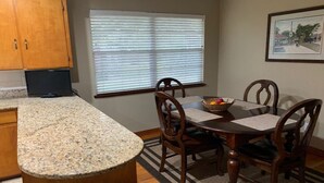 Una cocina con encimeras de granito, armarios de madera, una mesa de comedor con sillas y una ventana con persianas.