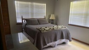 Un dormitorio con cama, mesita de noche, lámpara y dos ventanas con persianas.