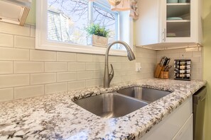 Een keuken met een dubbele spoelbak, witte metrotegels, een raam met een plant en een messenblok op het aanrecht.