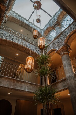An interior with a high ceiling, ornate railings, and hanging lights.