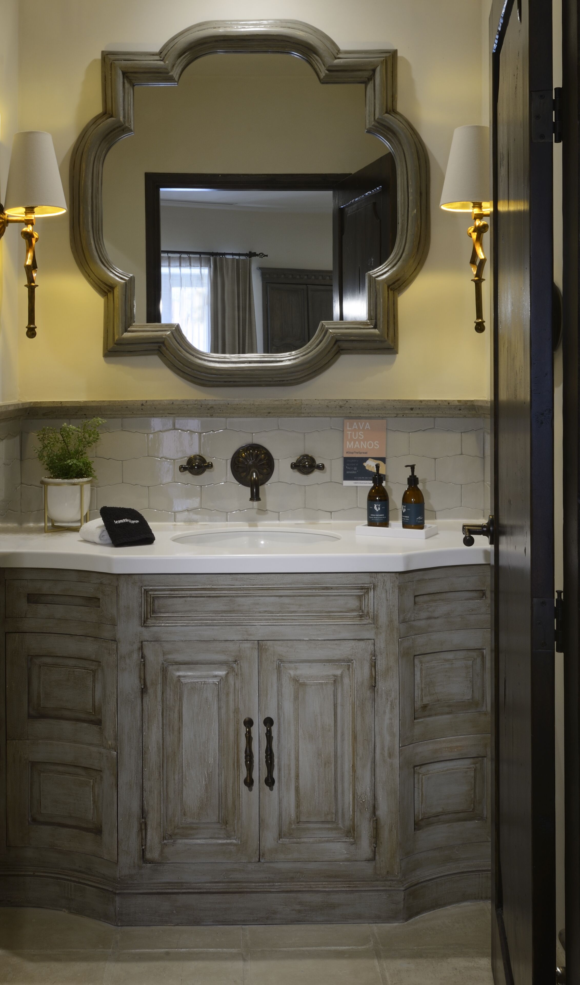 A bathroom with a large mirror, two wall-mounted lamps, a sink, and a cabinet with two doors.