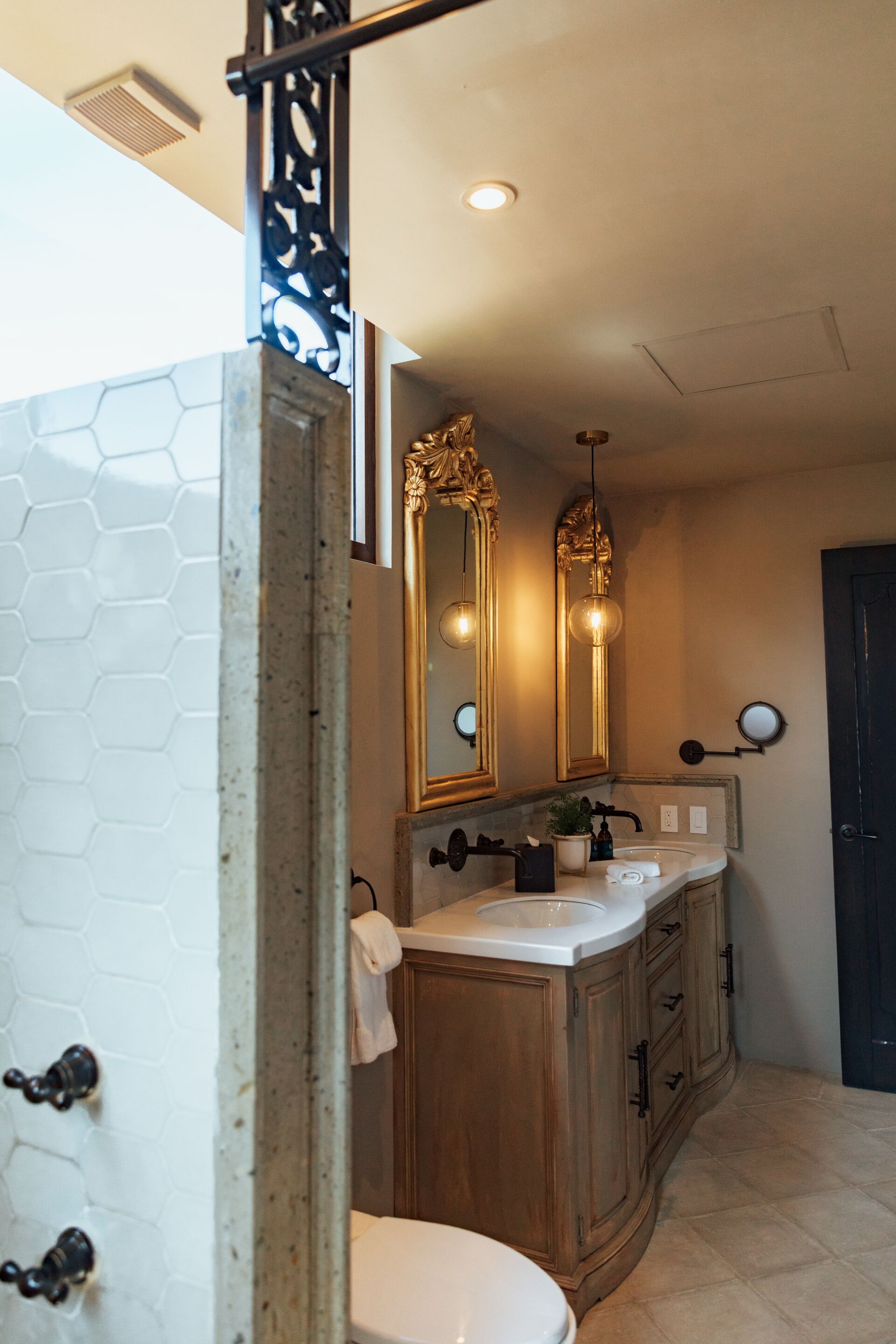 Une salle de bain avec des toilettes blanches, un meuble-lavabo en bois, deux miroirs et un mur recouvert de carreaux hexagonaux.