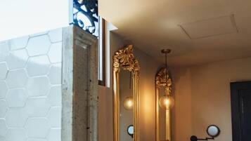 Une salle de bain avec des toilettes blanches, un meuble-lavabo en bois, deux miroirs et un mur recouvert de carreaux hexagonaux.