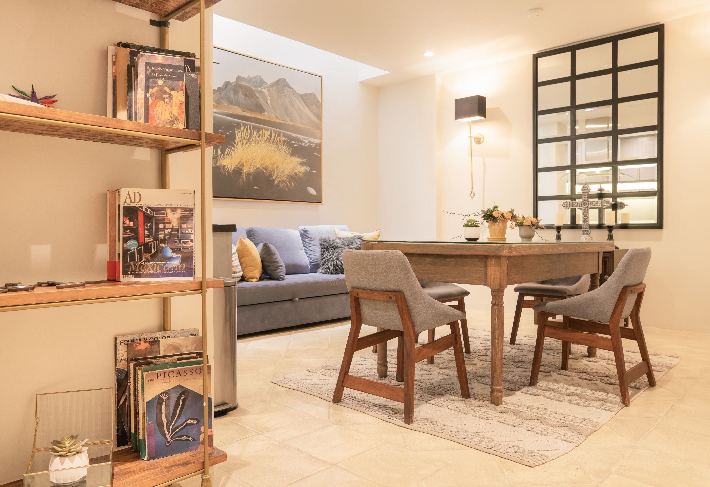 A modern living room with a sofa, two wooden chairs, a coffee table, and a bookshelf with books and decorative items.