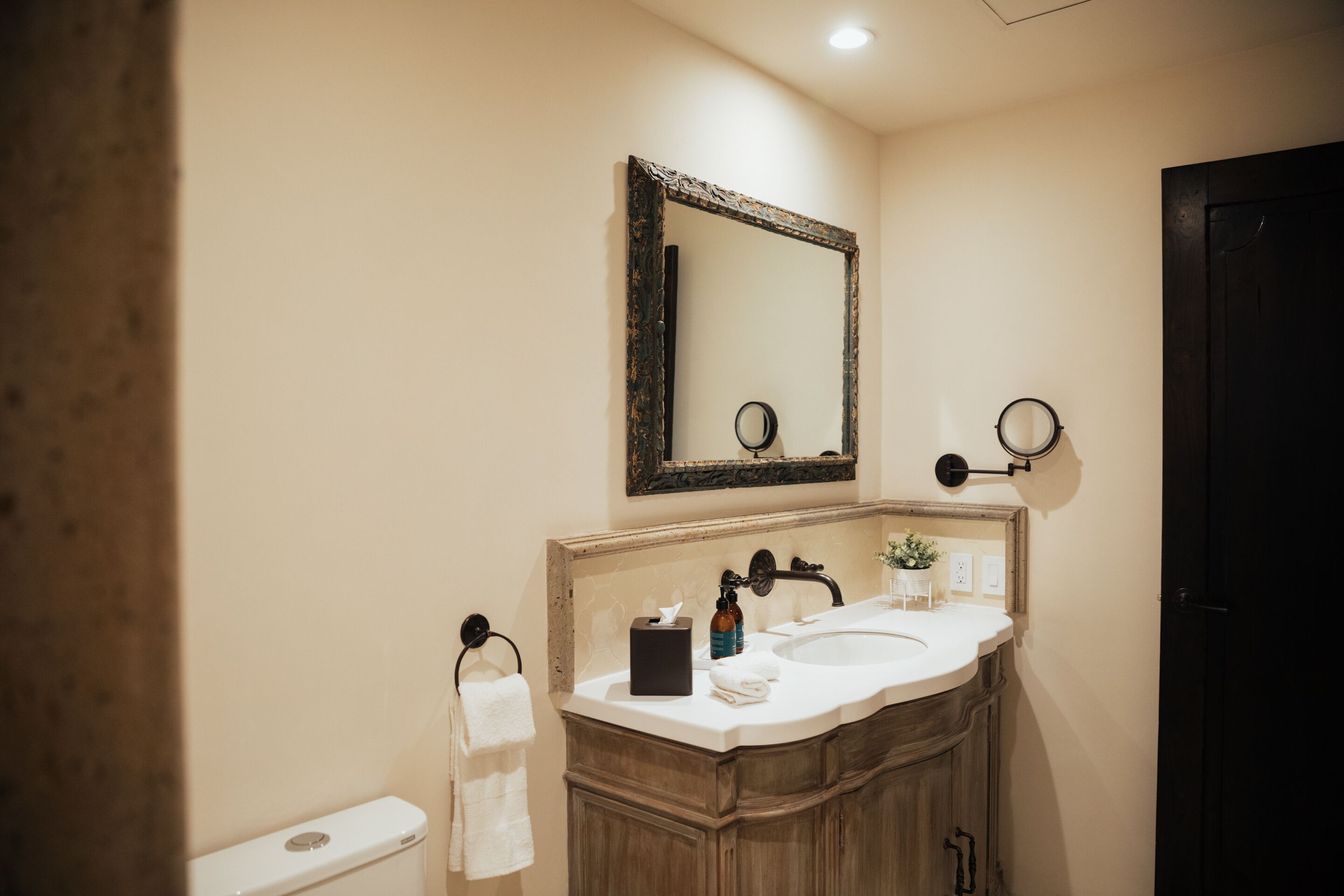 A bathroom with a wooden vanity, a white sink, a mirror, and a toilet.