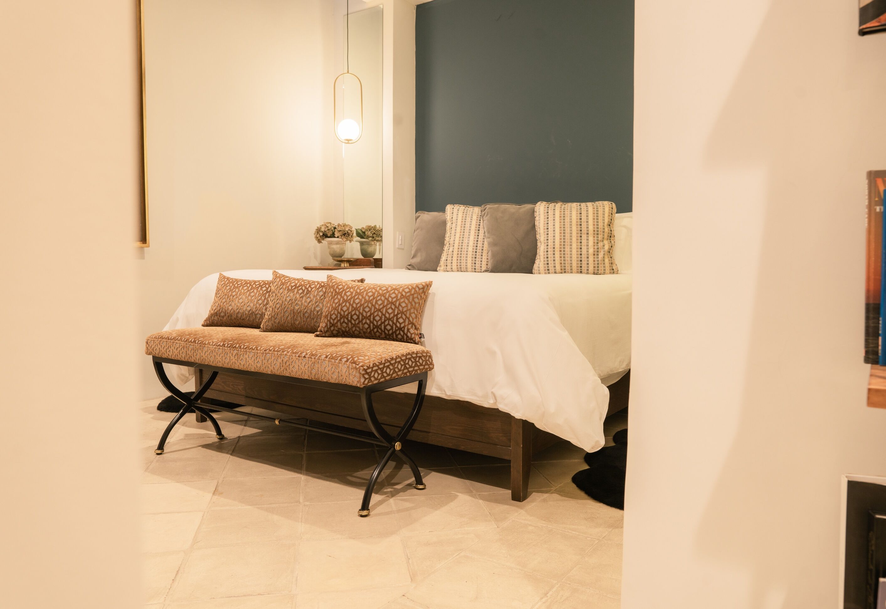 A neatly arranged bedroom with a bed, a bench, and a bedside table with flowers.