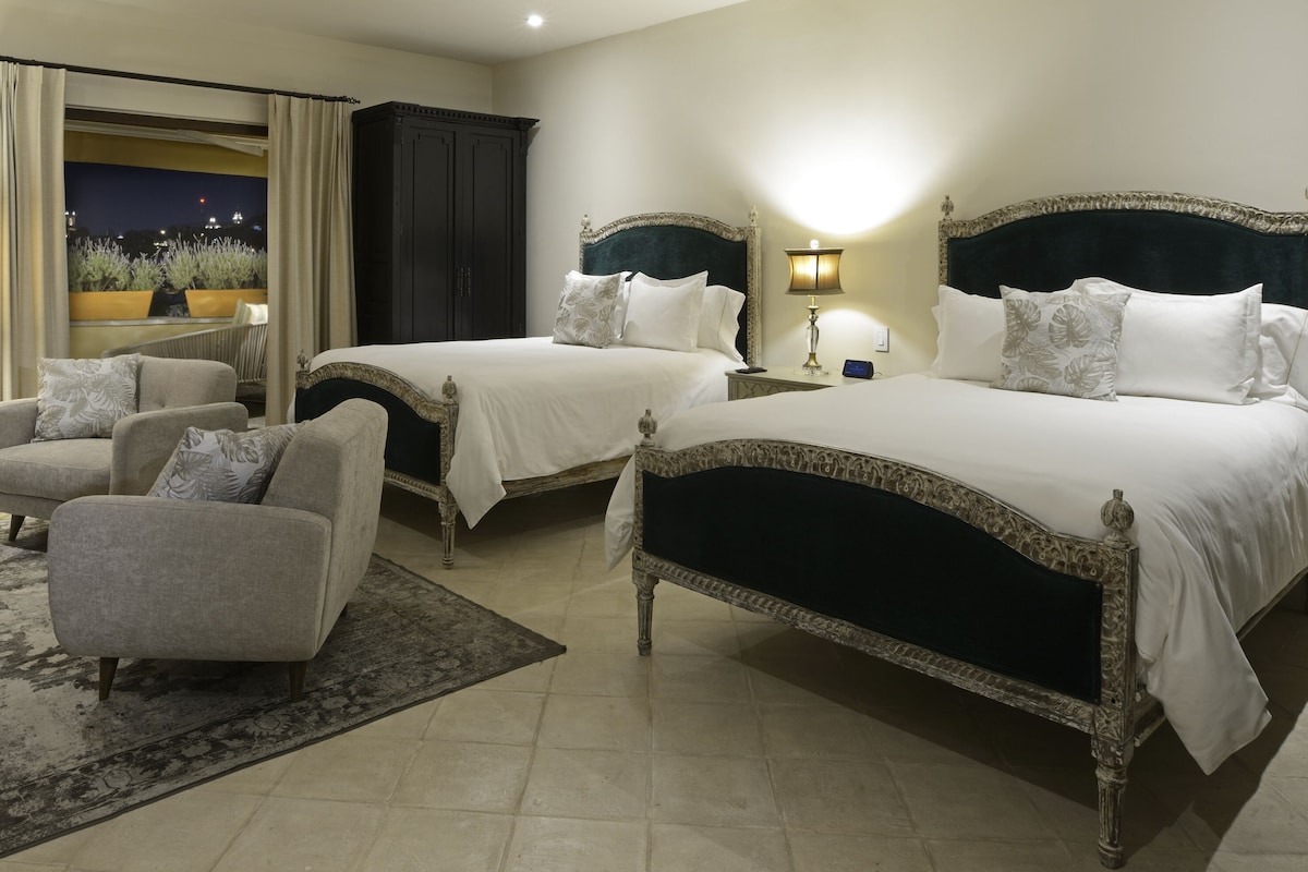 Ein Hotelzimmer mit zwei Betten, einer Sitzecke mit einem Sessel, einem Nachttisch, einer Lampe und Blick auf den Nachthimmel.