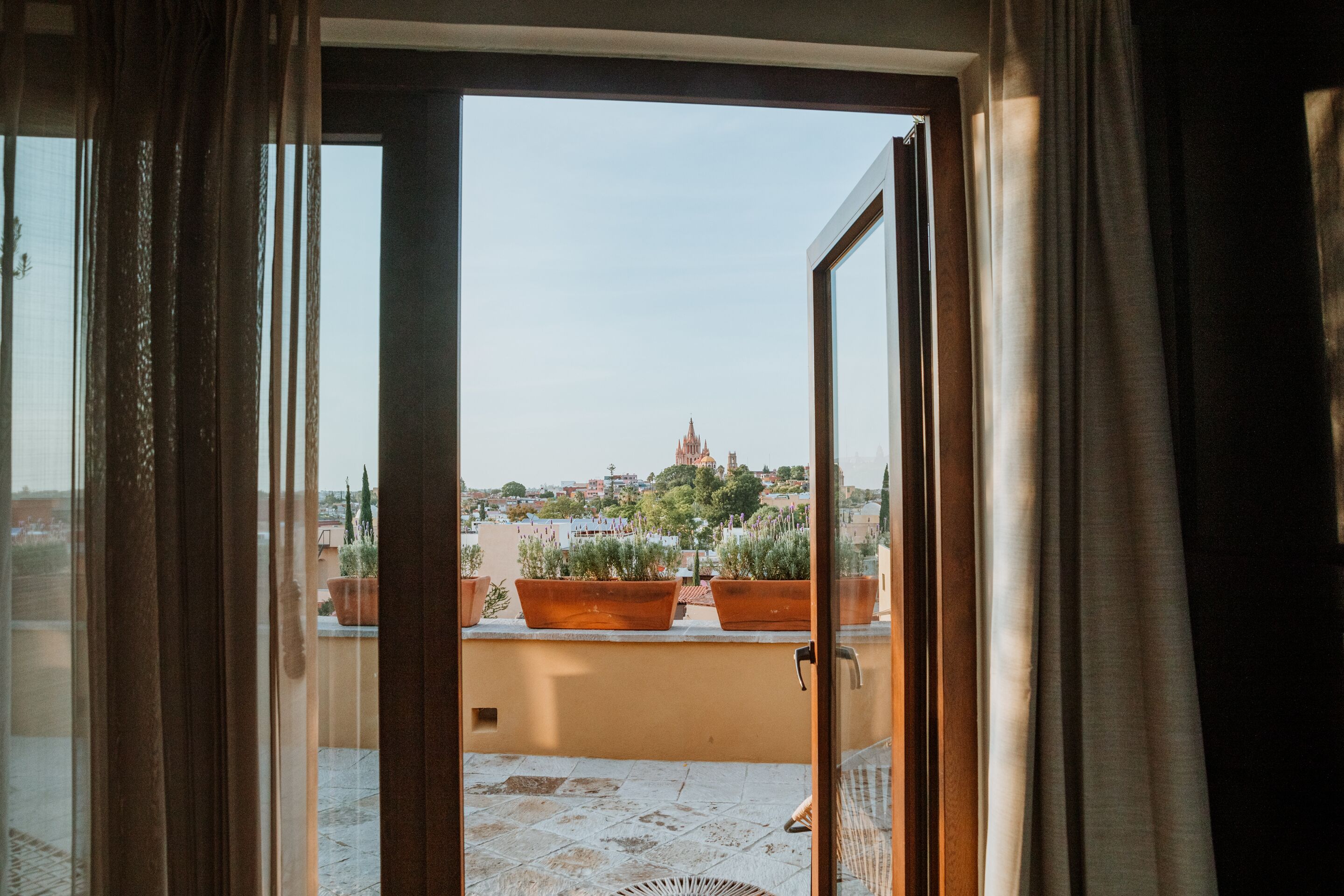 A view from a balcony with terracotta planters and a metal chair, overlooking a cityscape with a prominent church.