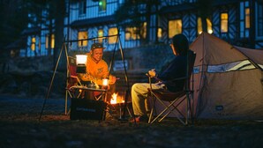 Two people sitting at a campfire with a tent and a building in the background. - Guest House Lamp Bungo Ohno - Hostel (Bungoono)