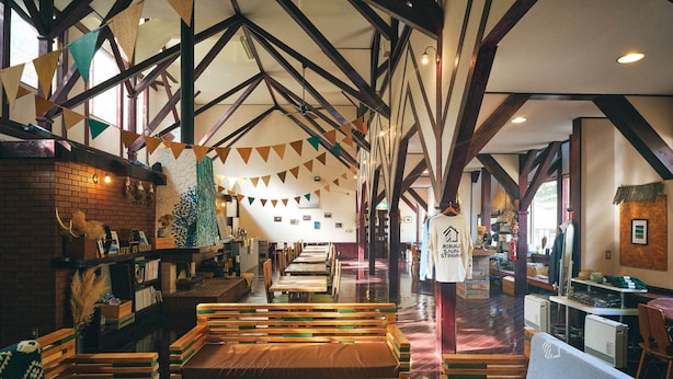 A spacious restaurant with wooden benches and tables, high ceilings with exposed beams, and a brick wall on one side. - Guest House Lamp Bungo Ohno - Hostel (Bungoono)