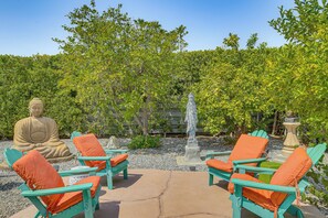 A serene outdoor seating area with a Buddha statue, a fountain, and lush greenery.