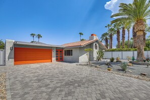 Una propiedad residencial con puerta de garaje roja, fachada de piedra y entrada pavimentada.