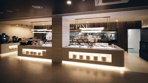 Un moderno vestíbulo de hotel con una recepción central y un restaurante visible llamado 'Pine'.