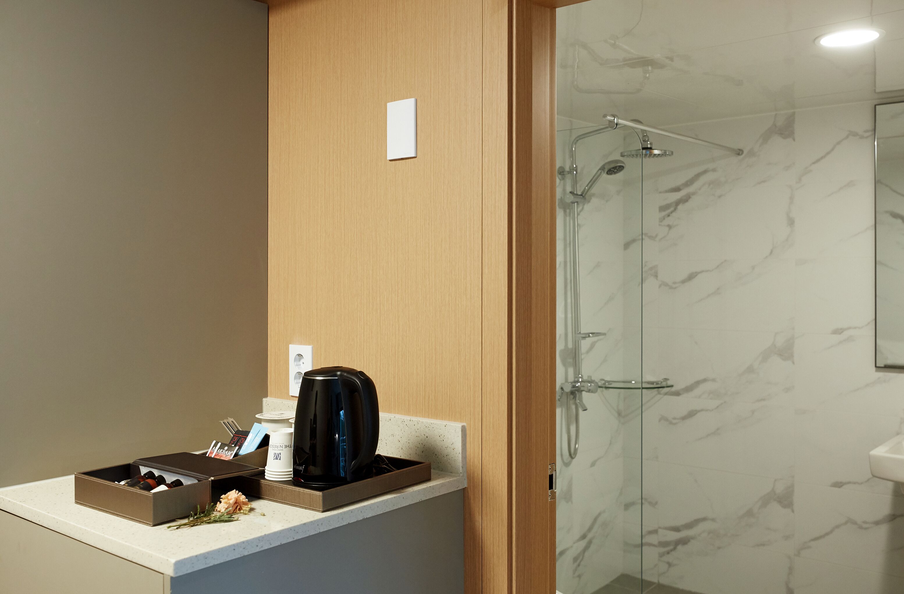 A modern bathroom with a marble shower, a coffee maker, and a box of wine glasses.