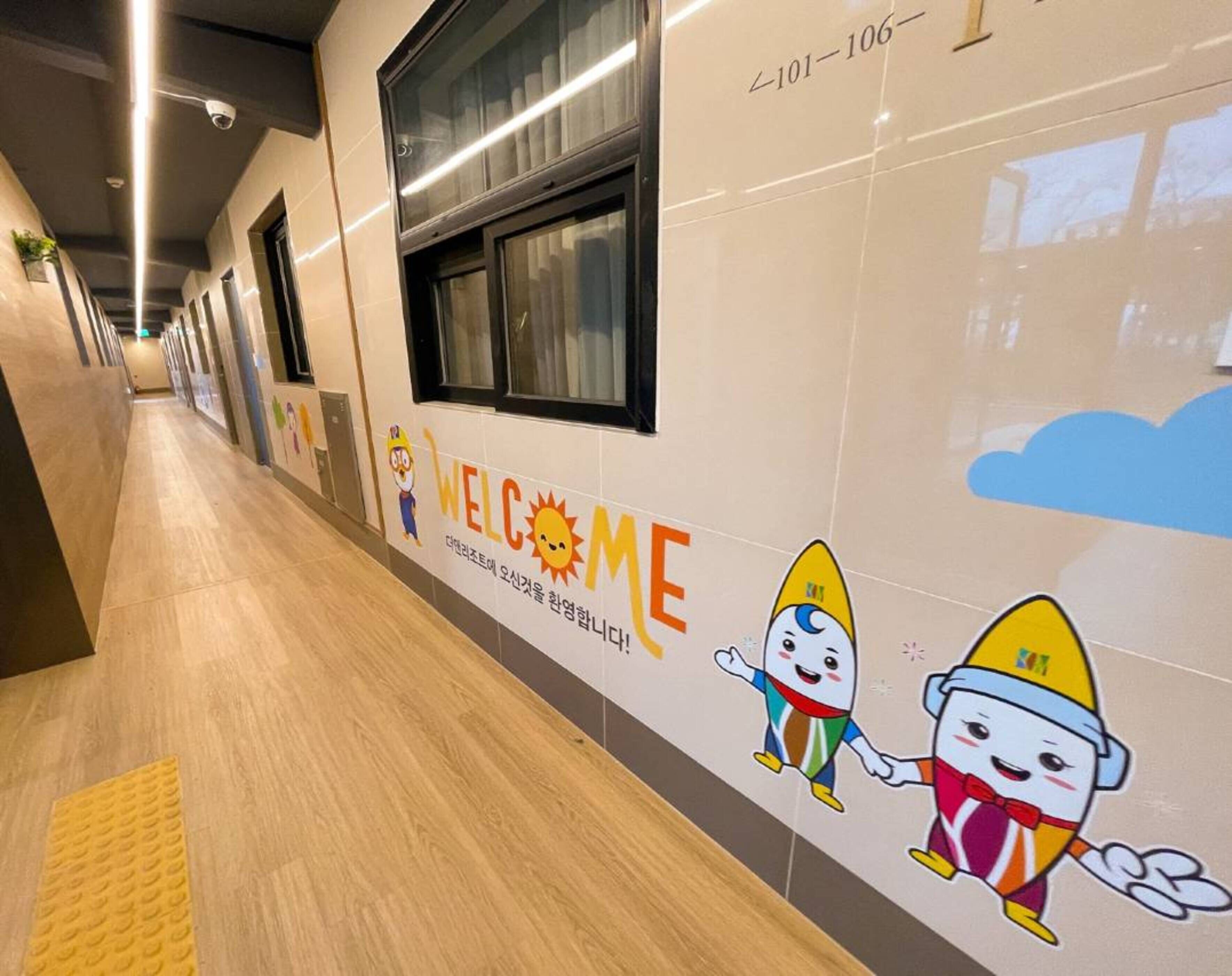 Un pasillo con un cartel que dice 'WELCOME' y personajes de dibujos animados, con una pared de azulejos y piso de madera.