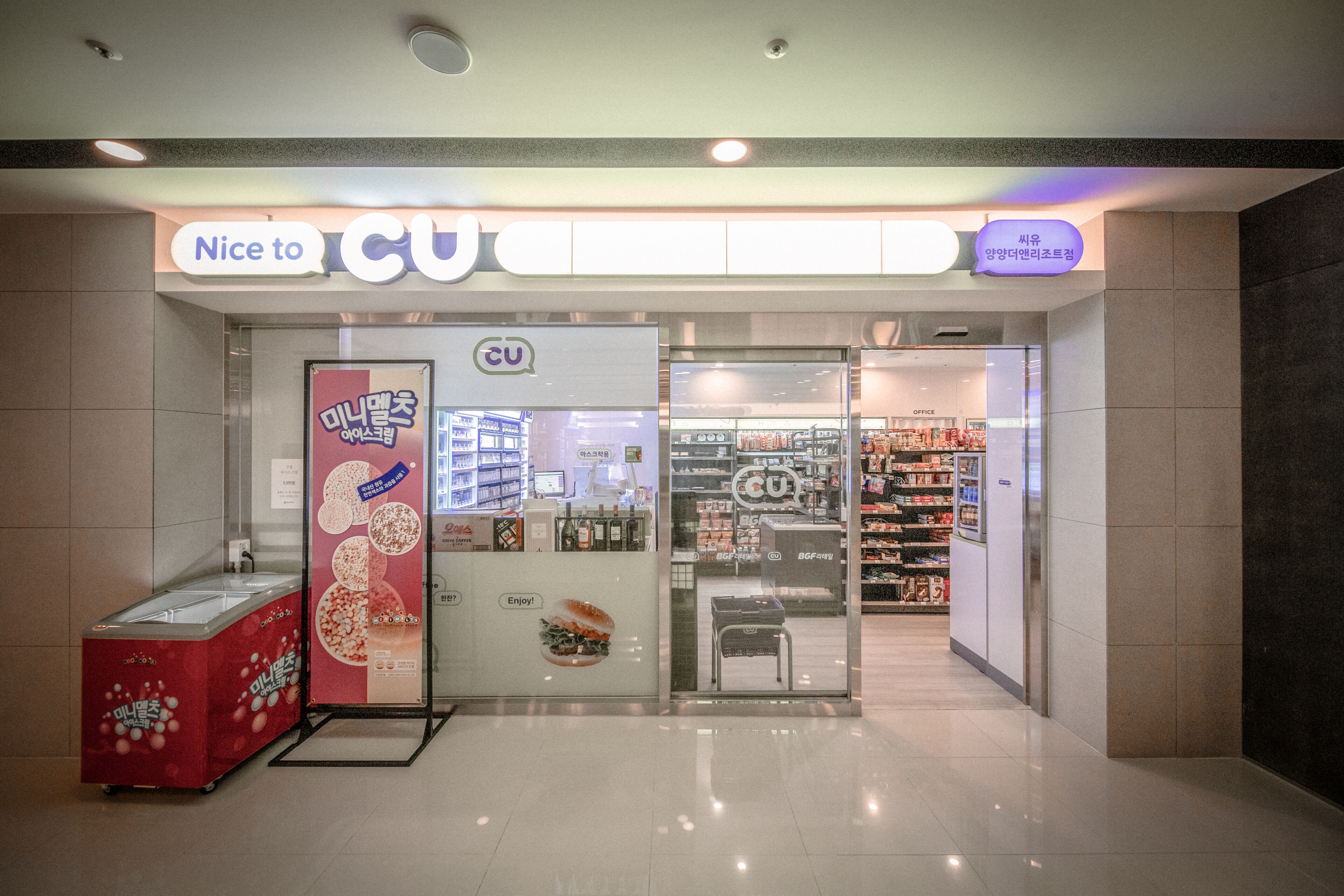 A CU store with a glass entrance, a refrigerated display, and a sign reading "Nice to CU".