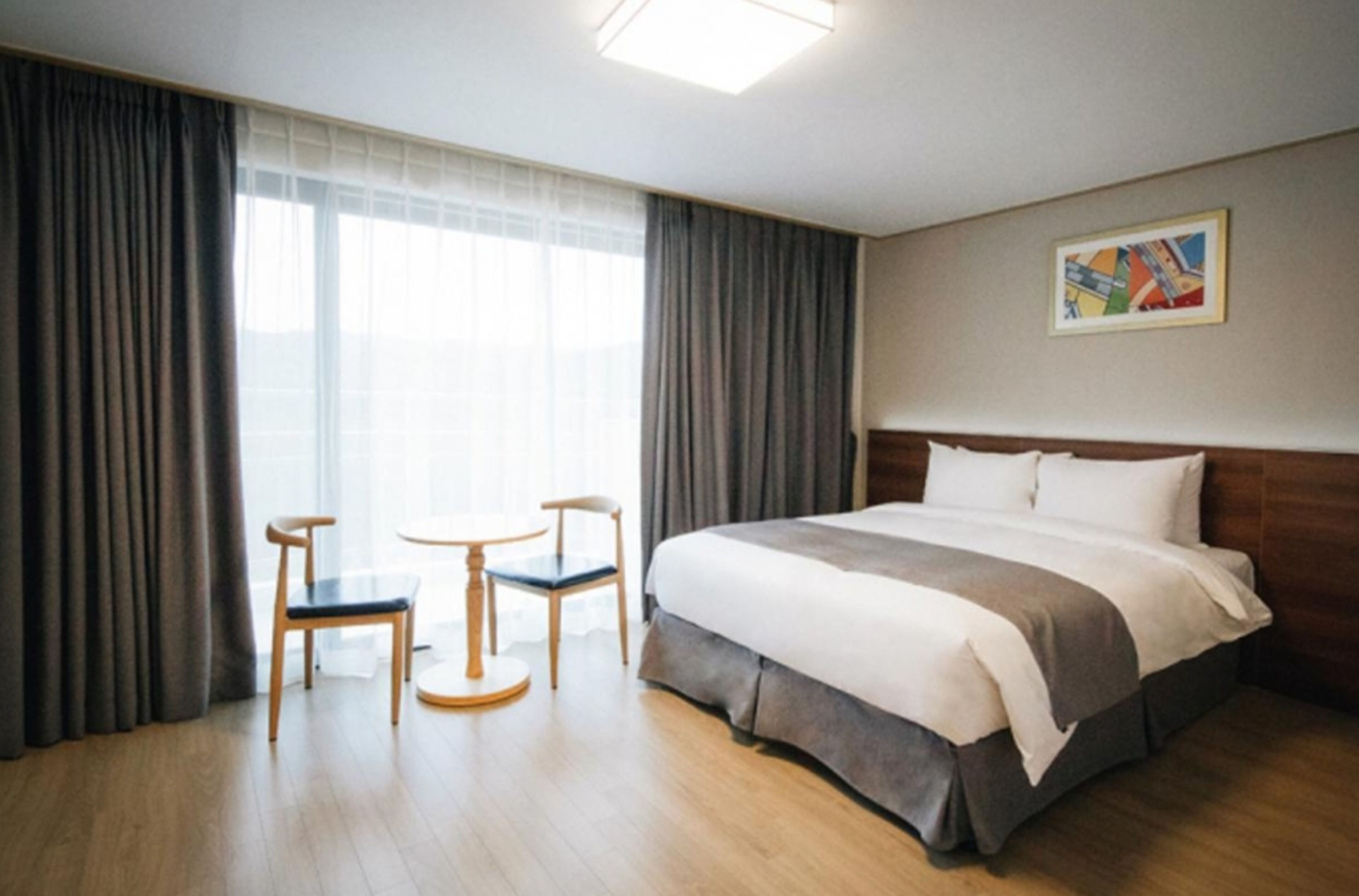 A hotel room with a large bed, two chairs, a small table, and a painting on the wall.