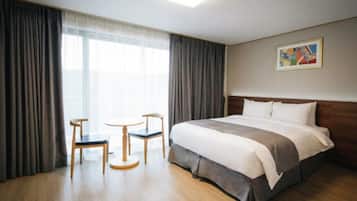 A hotel room with a large bed, two chairs, a small table, and a painting on the wall.