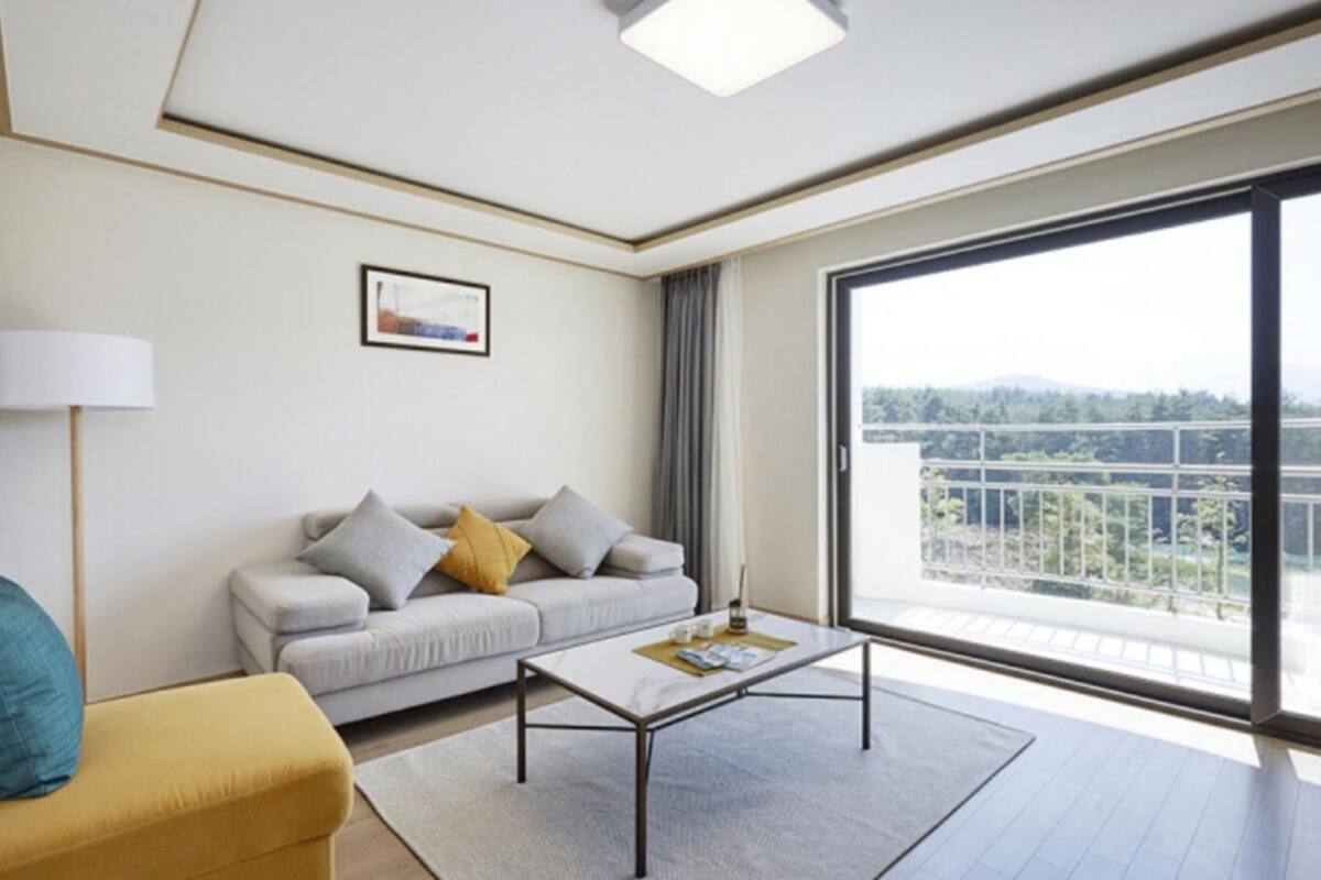 Ett modernt hotellrum med en soffa, ett soffbord, en lampa och ett stort fönster med utsikt över balkongen.