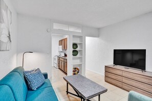 Una sala de estar moderna con un sofá, una mesa de centro, un televisor y una cocina al fondo.