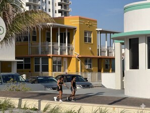 Un edificio giallo con balconi, una struttura bianca con decorazioni verdi e auto parcheggiate.