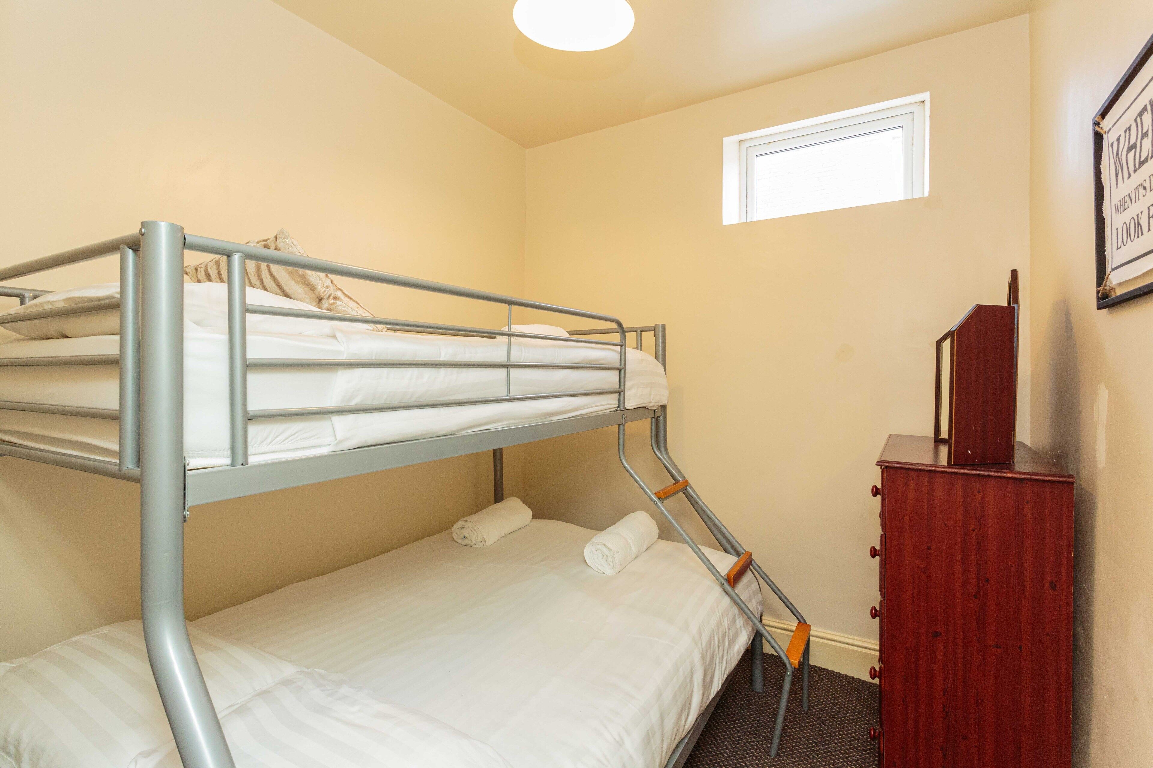 A bunk bed room with a small window and a wooden dresser.