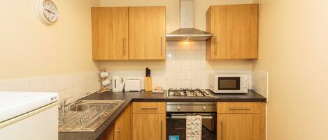 Een kleine keuken met houten kastjes, een roestvrijstalen afzuigkap, een magnetron, een oven en een vaatwasser.