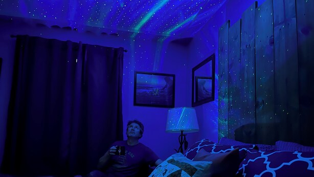Une pièce avec un lit, une lampe fixée au mur et une fenêtre avec des rideaux.