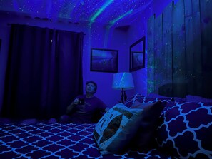 A room with a bed, a wall-mounted lamp, and a window with curtains.