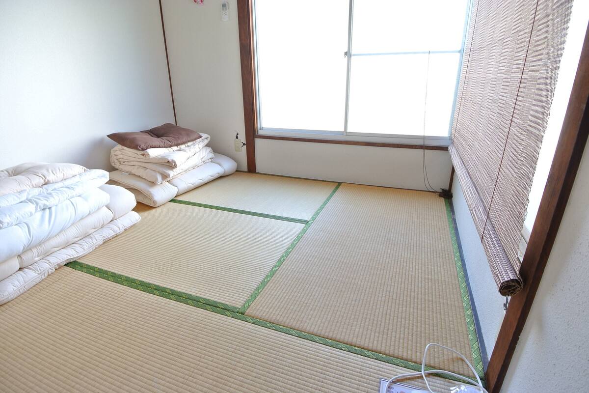 A tatami mat room with a window, a bed with pillows, and a wall socket.