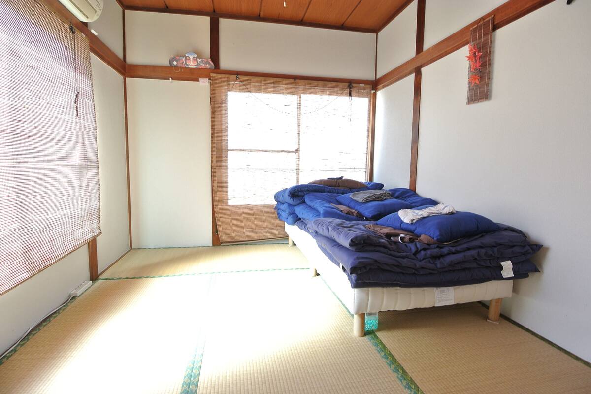A traditional Japanese room with tatami flooring, a bed with blue bedding, and a shoji screen door.