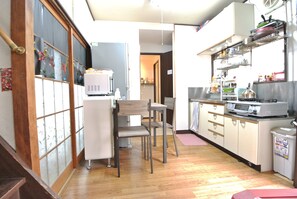 Une cuisine compacte équipée d’un réfrigérateur, d’un four à micro-ondes et de divers appareils de cuisine. Elle comprend deux chaises et une petite table à manger. La cuisine est dotée d’un plancher en bois et offre une vue sur la pièce adjacente grâce à une porte vitrée.