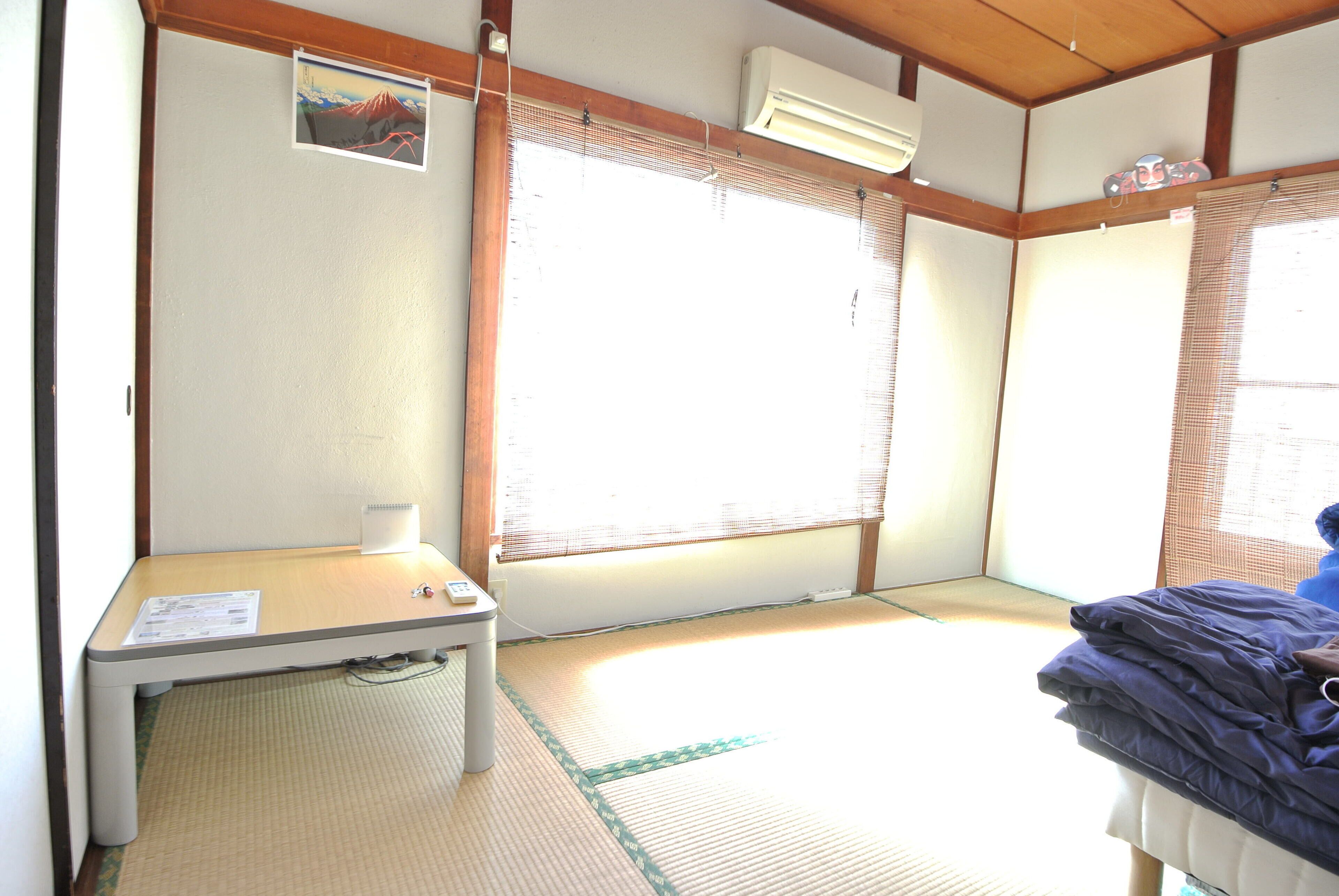 A room with tatami flooring, a futon bed, a small table with a lamp, and a picture on the wall.