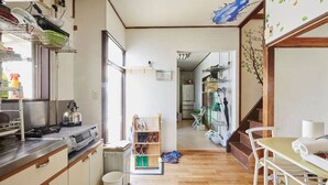 A compact kitchen with wooden cabinets, a sink, and a kettle. There is a small dining area with a table and chairs. - Nishiogi House Maipenrai (Tokyo)