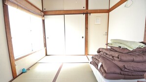 A traditional Japanese room with tatami flooring, a futon bed, and sliding doors. - Nishiogi House Maipenrai (Tokyo)
