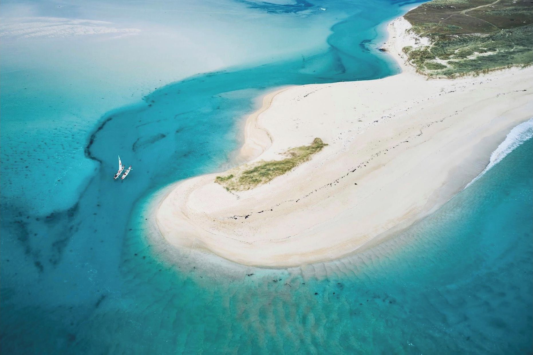 Vista aérea de una playa con aguas turquesas cristalinas, una orilla arenosa y una pequeña zona de vegetación.