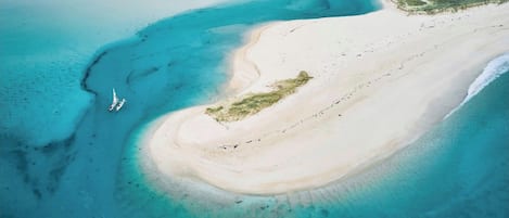 Vista aérea de una playa con aguas turquesas cristalinas, una orilla arenosa y una pequeña zona de vegetación.