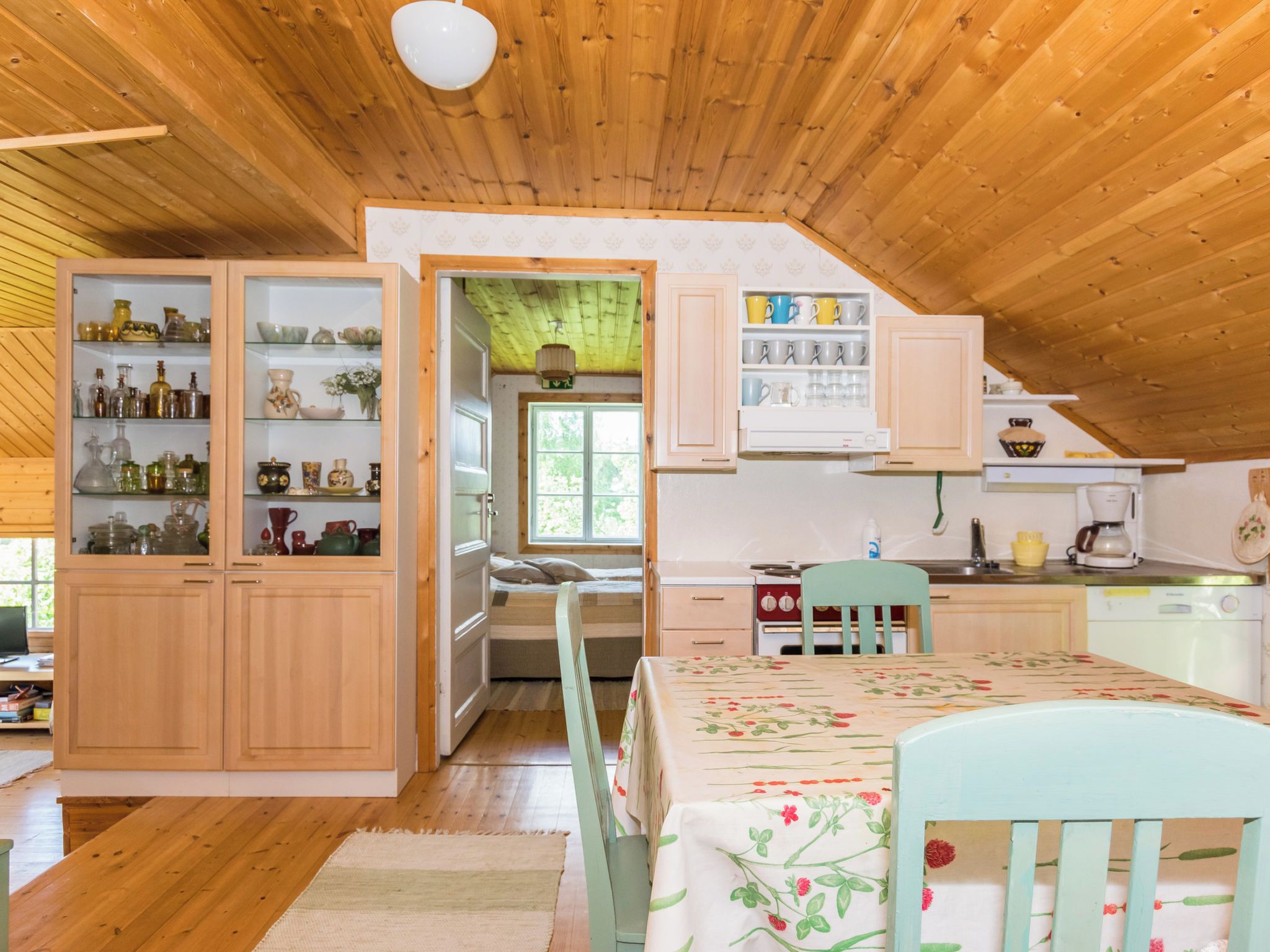 A cozy kitchen with wooden cabinets, a dining table with floral tablecloth, and a view of the outdoors.