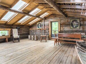 Een rustiek blokhutinterieur met houten vloeren, een hoog plafond met dakramen, en een eethoek met banken en stoelen.