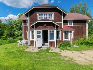 A two-story wooden house with a front porch, a visible entrance, and a small garden area with chairs. - Lamminkangas by Interhome (Saarijärvi)