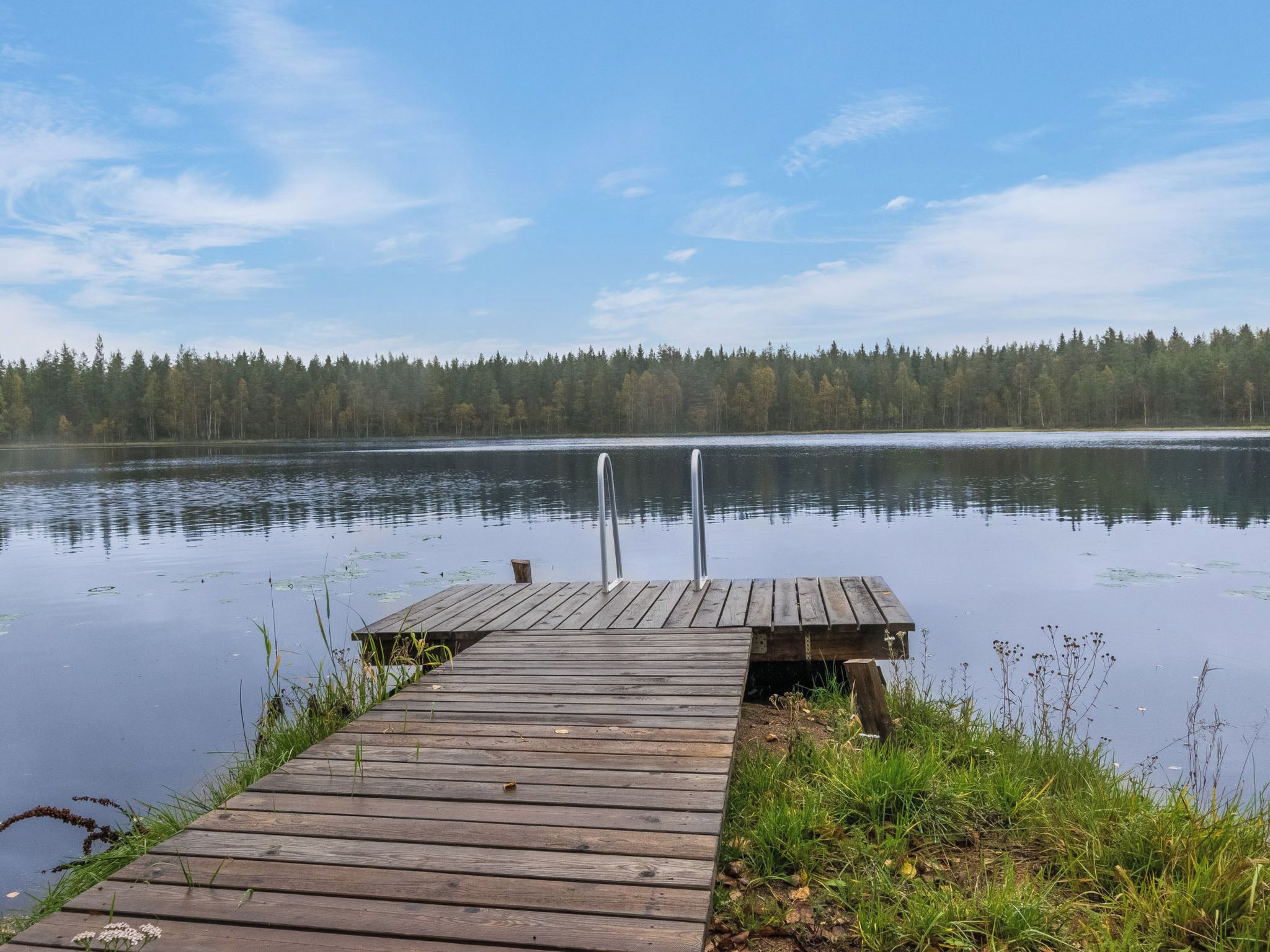 A wooden dock extending into a calm lake, surrounded by a forest.