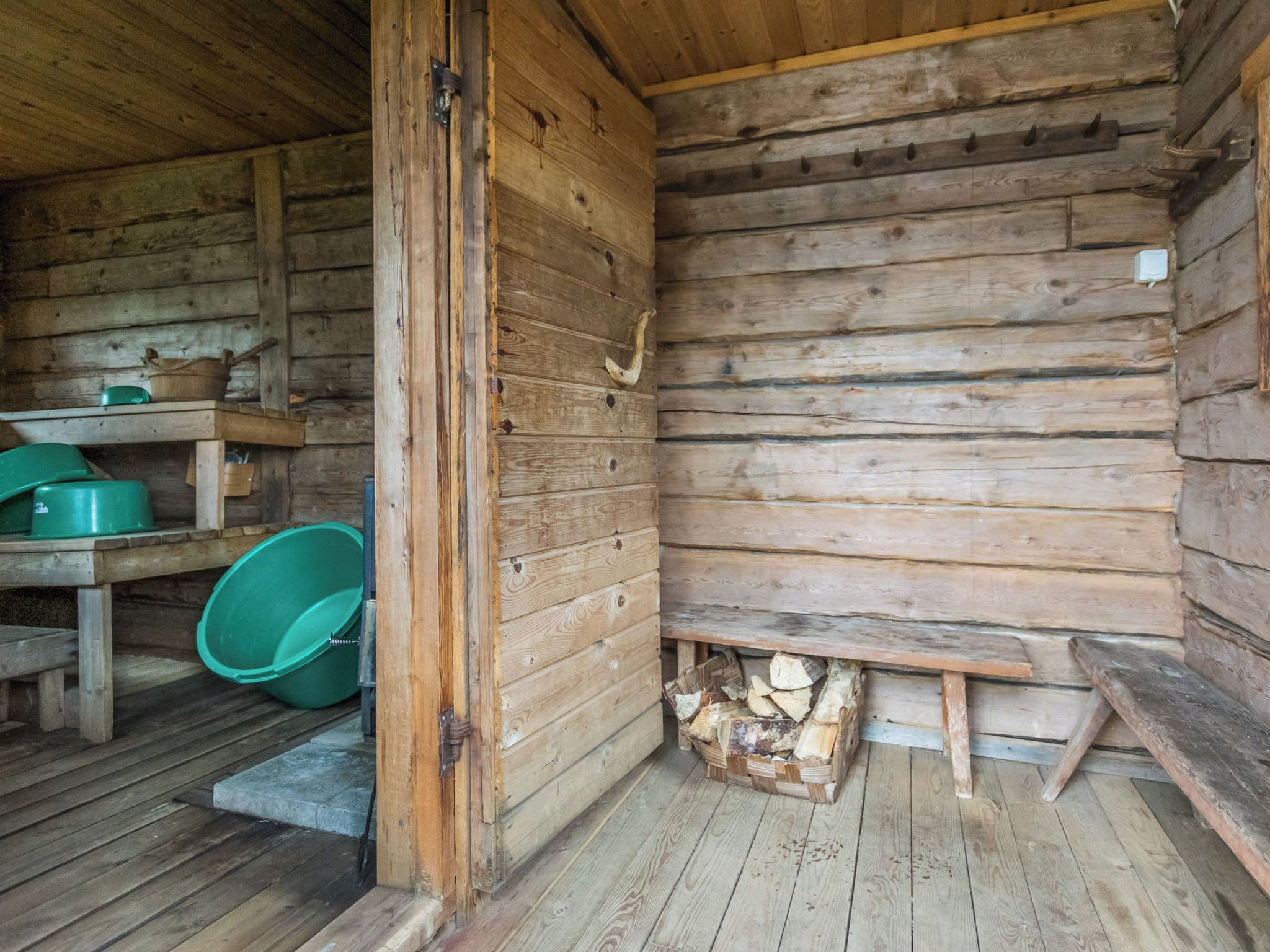 L’intérieur d’un chalet rustique en bois, avec un banc en bois, un seau vert et une pile de bois de chauffage.
