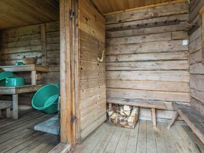 Een rustiek houten chalet van binnen, met een houten bankje, een groene emmer en een stapel haardhout.