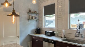 Une cuisine dotée de plans de travail en granit, de meubles en bois foncé, d’un lave-vaisselle, d’une machine à café et d’un grille-pain. On y trouve également des luminaires suspendus, une fenêtre avec vue et une étagère contenant des ustensiles de cuisine.