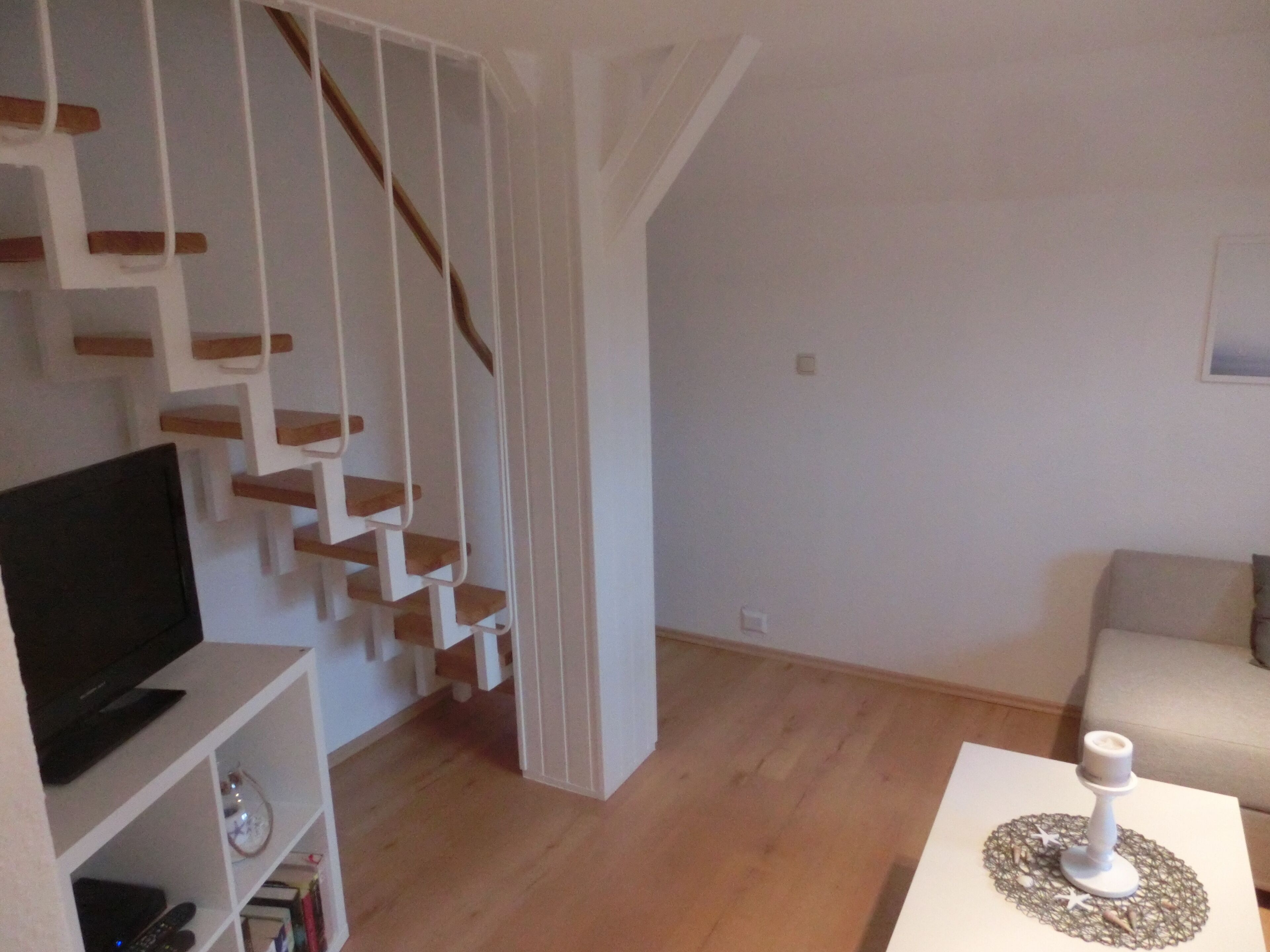 A modern living room with a staircase, a flat-screen TV, and a white table with a candle.