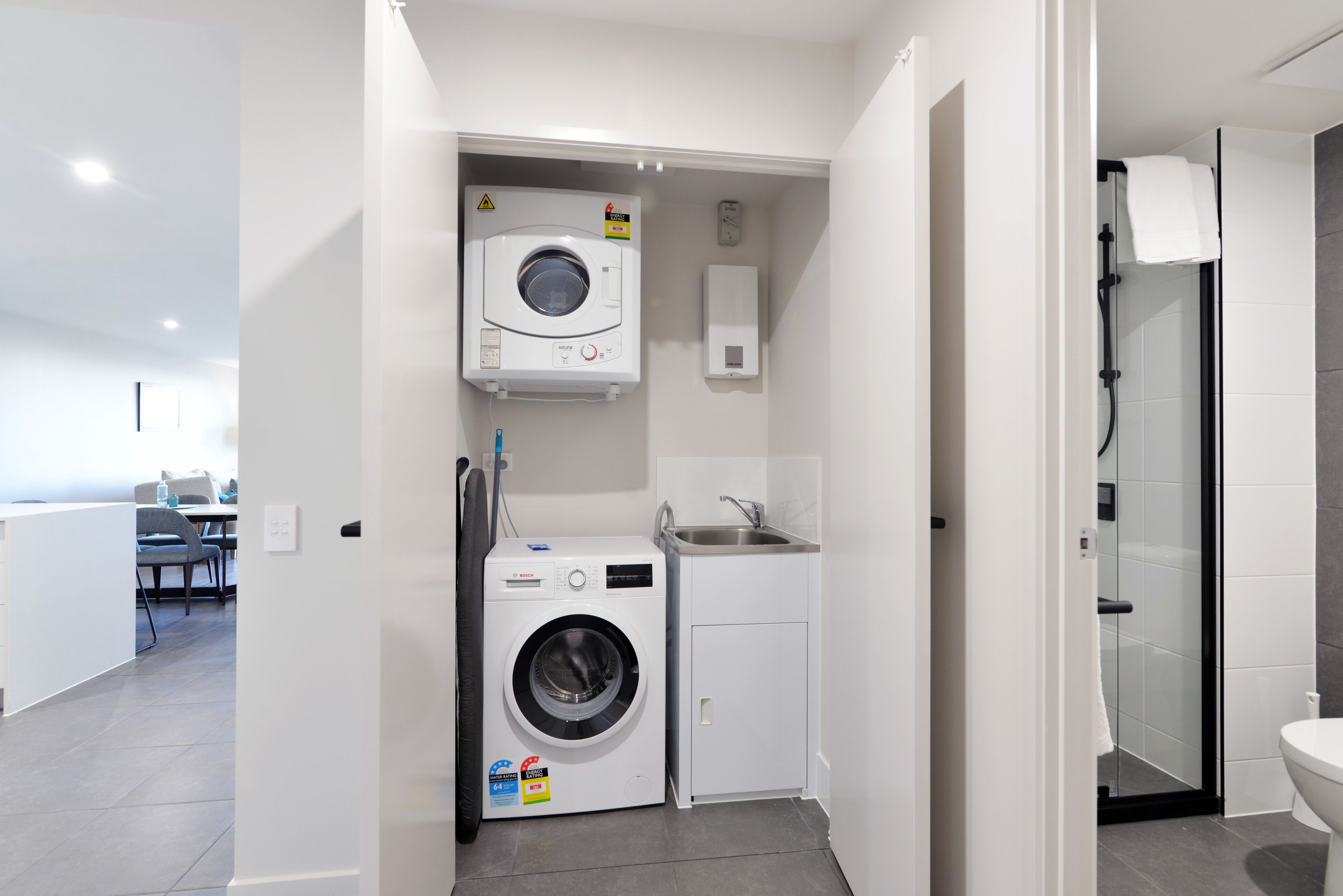 A compact laundry room with a washing machine, a small sink, and a glass shower enclosure.