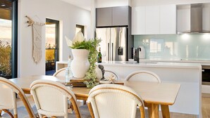 A modern kitchen with white cabinetry, a central island, and wicker chairs. - Hedge Apartments by CLLIX (Buddina)