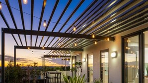 An outdoor dining area with a pergola, potted plants, and a table set for two. - Hedge Apartments by CLLIX (Buddina)